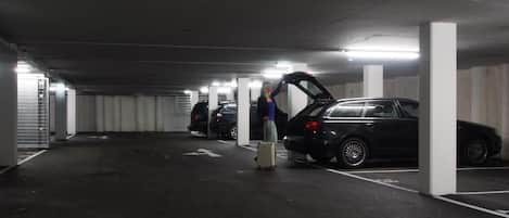 A parking garage with multiple cars and a person standing next to a car with the hood open.