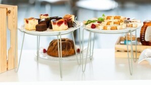 Ein Essbereich mit runden Tischen, einer Auswahl an Desserts und Blick auf Grünflächen.