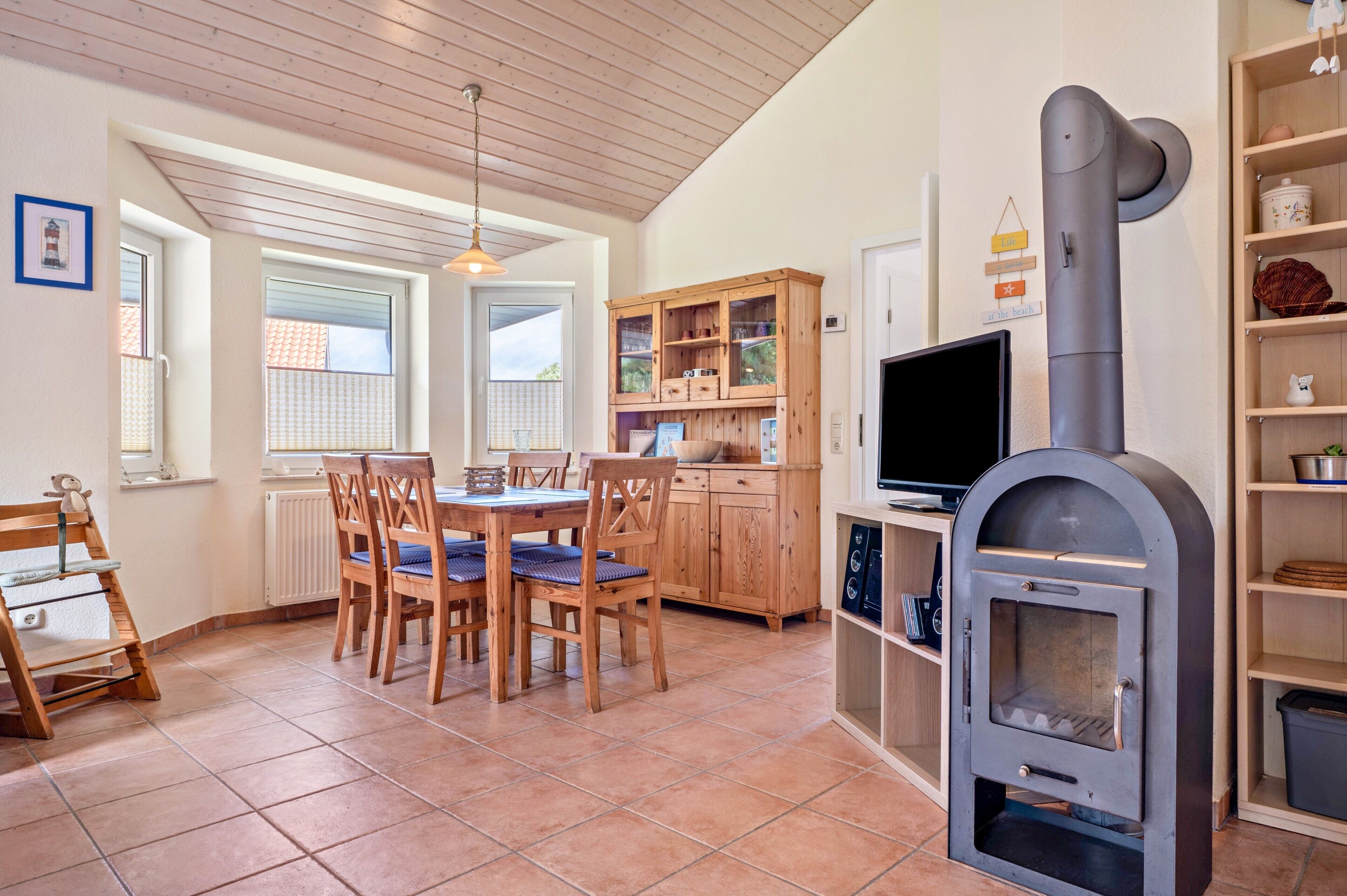Una cocina con una mesa de comedor, sillas, un armario de madera, un televisor y un horno a leña.