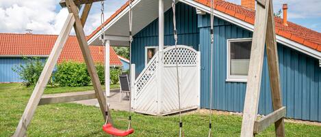 A wooden swing set with two swings in front of a blue house with a red roof.