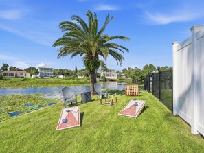 Un jardin avec un étang, deux fauteuils Adirondack, un palmier et une clôture blanche.
