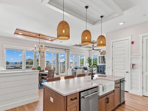 Une cuisine moderne dotée d’un grand îlot central, de luminaires suspendus et offrant une vue sur l’extérieur.