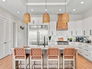 Une cuisine moderne dotée d’un îlot central, d’appareils électroménagers en acier inoxydable et de luminaires suspendus.