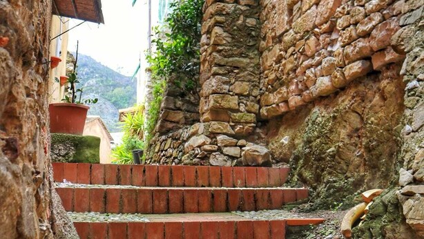 Un escalier étroit en pierre, surmonté d’une arche rustique, mène à un bâtiment à la façade en pierre.