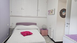 Une chambre à coucher comprenant un lit, une table de chevet, une commode, un radiateur et une porte.