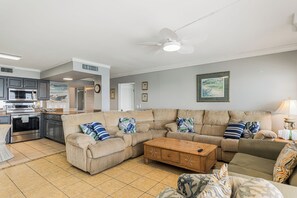 A living room with a sectional sofa, a wooden coffee table, and a kitchen area with appliances. - Summit Penthouse 3BR 3BA, Great Location! (Panama City Beach)