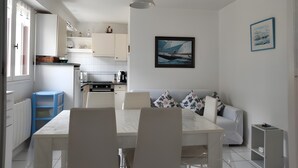 Eine moderne Küche mit weißen Schränken, einem Esstisch mit Stühlen, einem weißen Sofa und einer Deckenleuchte.