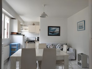 Eine moderne Küche mit weißen Schränken, einem Esstisch mit Stühlen, einem weißen Sofa und einer Deckenleuchte.
