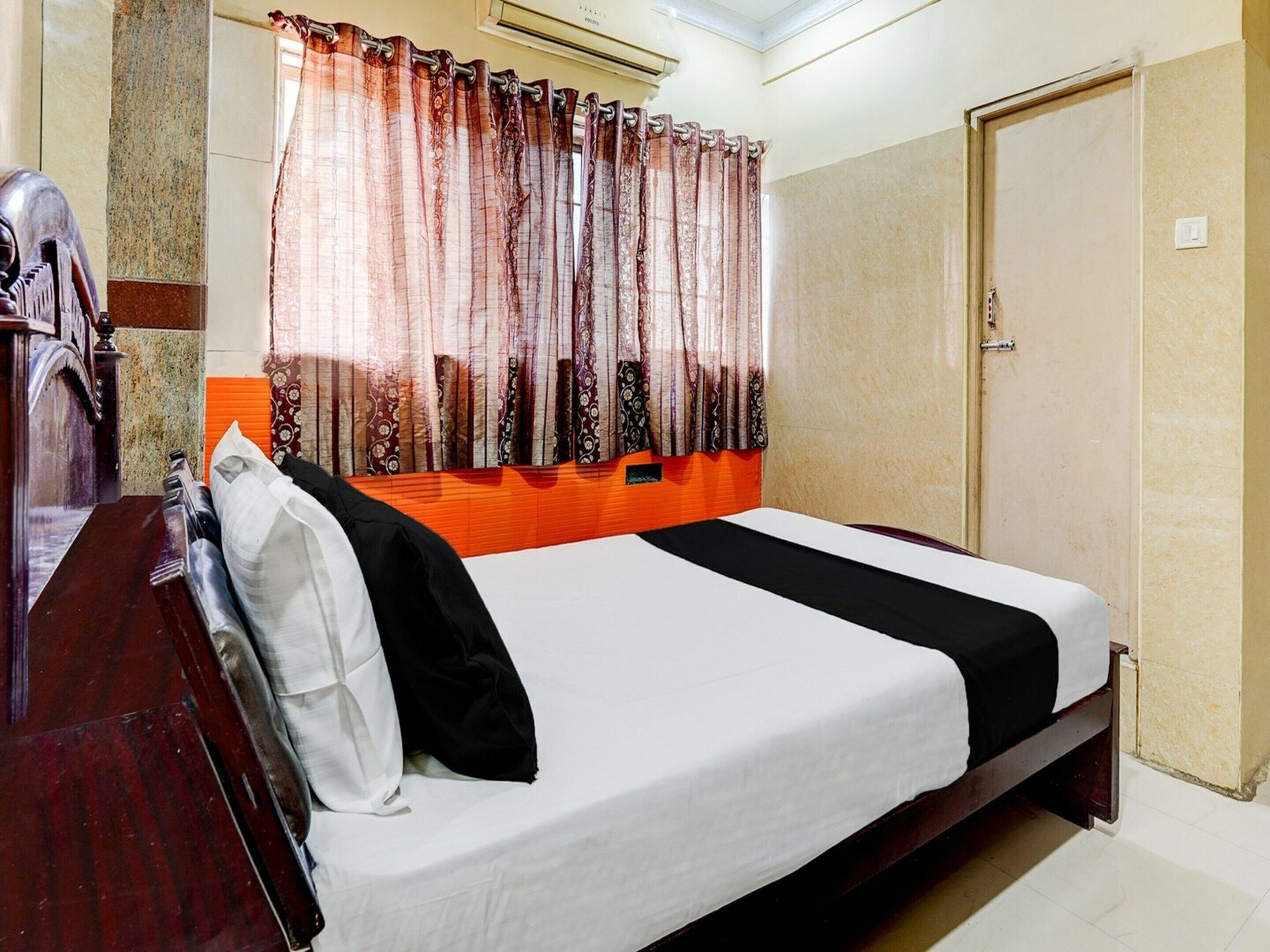 Una habitación de hotel con cama, armario, espejo y ventana con cortinas.