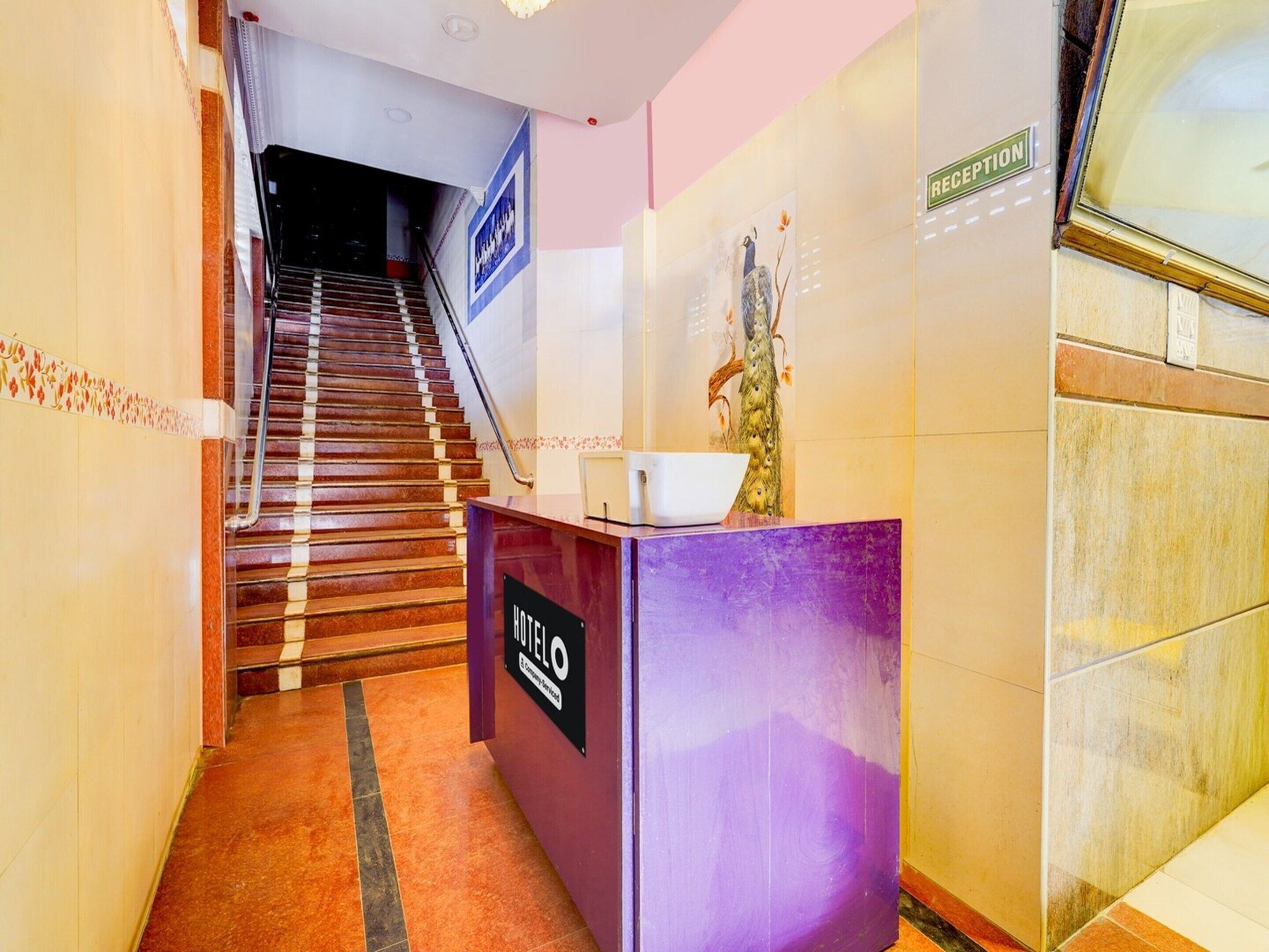A hotel reception desk with a sign, a staircase, and a reception area.