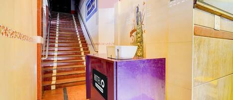 A hotel reception desk with a sign, a staircase, and a reception area.