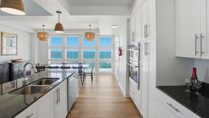 Cocina moderna con armarios blancos, encimera de granito y vista al océano.