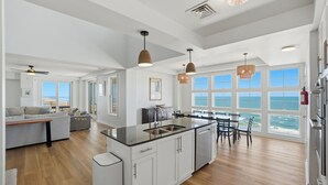 Una cocina amplia con una isla grande, armarios blancos y vista al océano.
