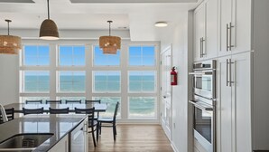 Una cocina con vista al océano, armarios blancos, un horno de acero inoxidable y una mesa de comedor con sillas.