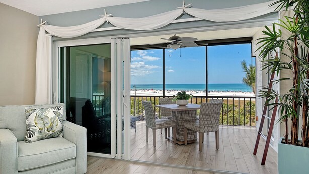 Un balcon avec vue sur la plage, des meubles en osier, un ventilateur de plafond et une plante en pot.
