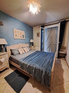 Un dormitorio con cama, mesitas de noche, cómoda, alfombra, puerta y lámpara.