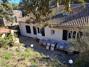 Una casa de dos pisos con techo de tejas, un porche cubierto con mobiliario exterior y una ventana pequeña.
