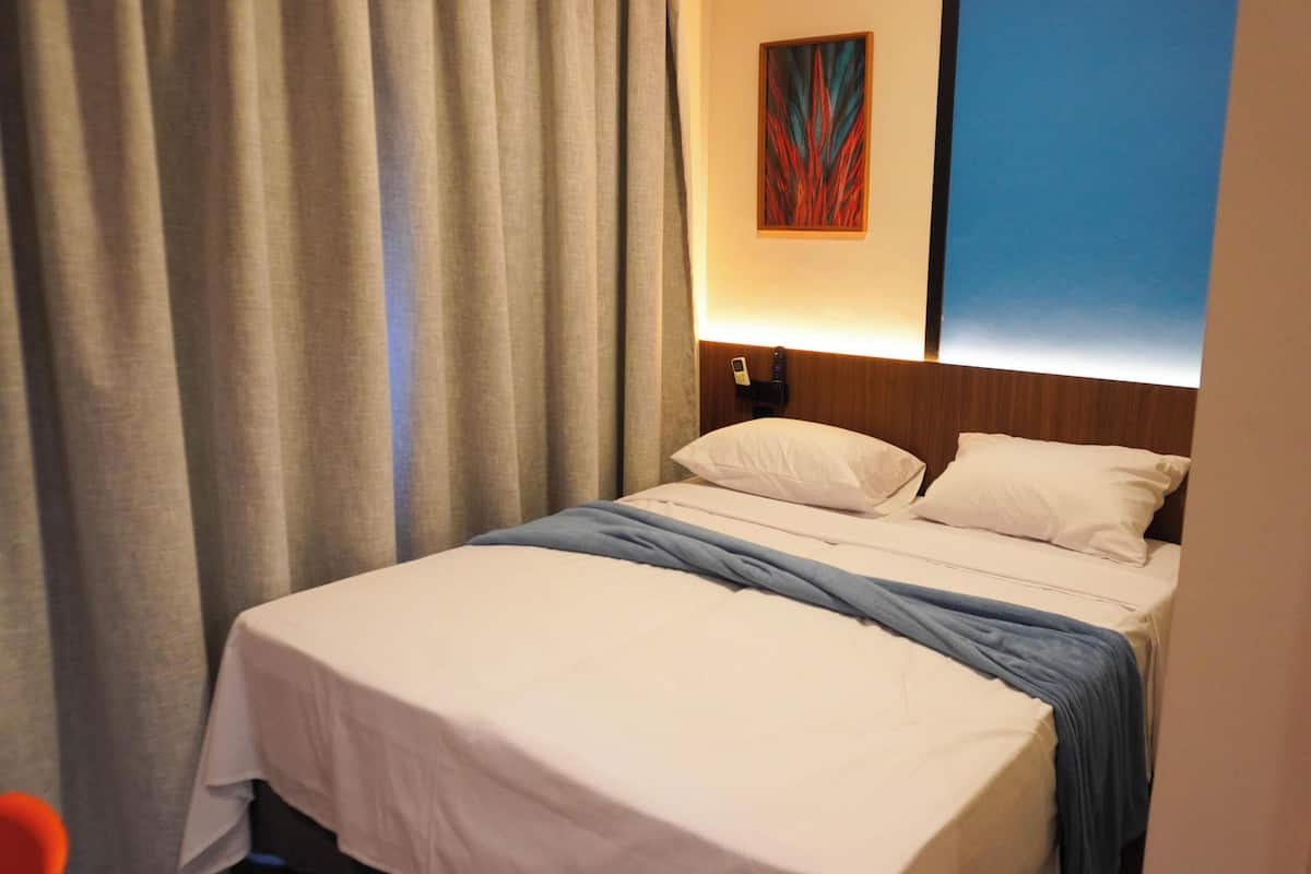 A hotel room with a bed, curtains, a painting, and a nightstand.