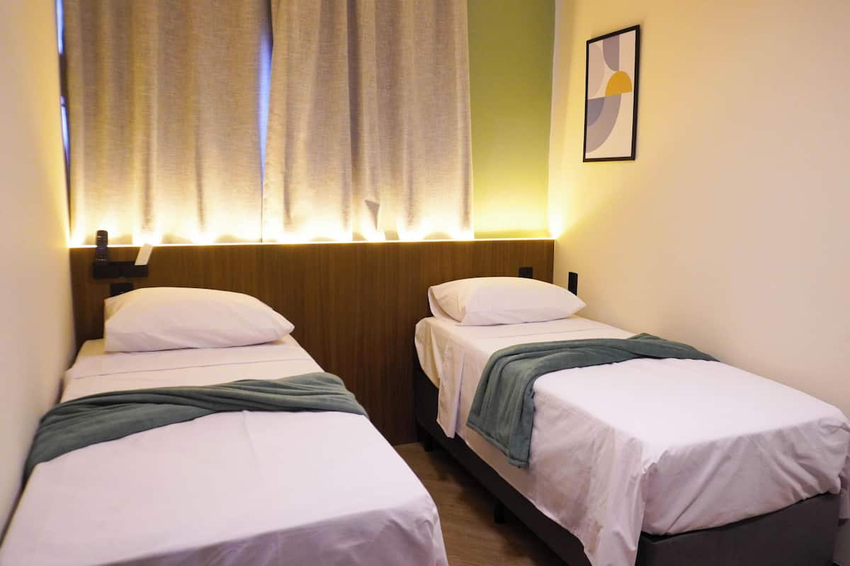 A room with two single beds, a wooden headboard, a window with curtains, and a framed picture on the wall.