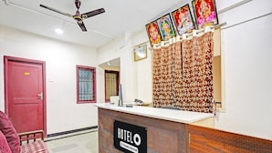 A hotel reception desk with a sign reading 'HOTEL COMPANY SERVICE,' a ceiling fan, and a red door.