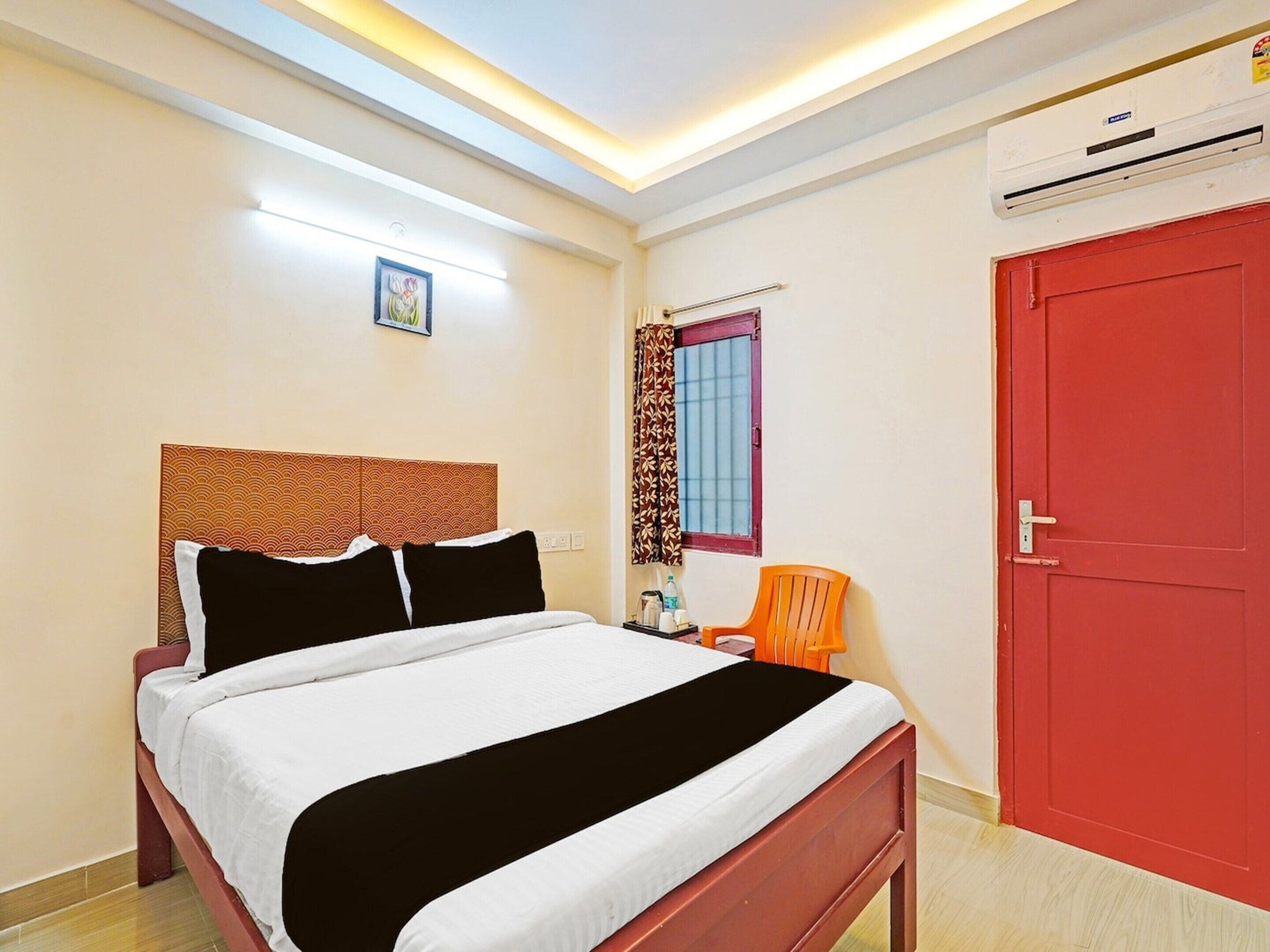 Un dormitorio con cama, ventana con cortinas, equipo de aire acondicionado y una puerta roja.