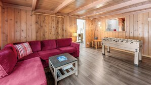 Een gezellige kamer met houten inrichting, een rode bank, een tafeltje en een tafelvoetbal.
