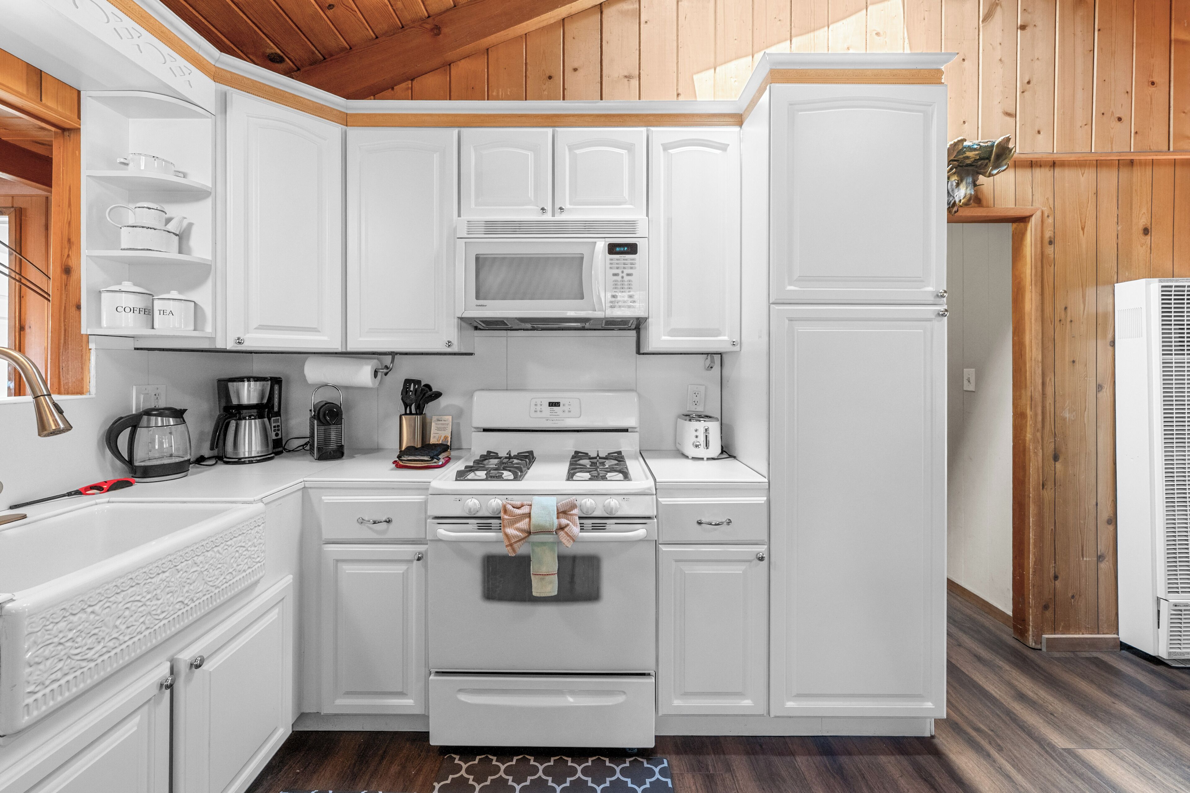 A compact kitchen with white cabinetry, a gas stove, a microwave, and a refrigerator.