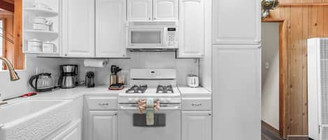 A compact kitchen with white cabinetry, a gas stove, a microwave, and a refrigerator.