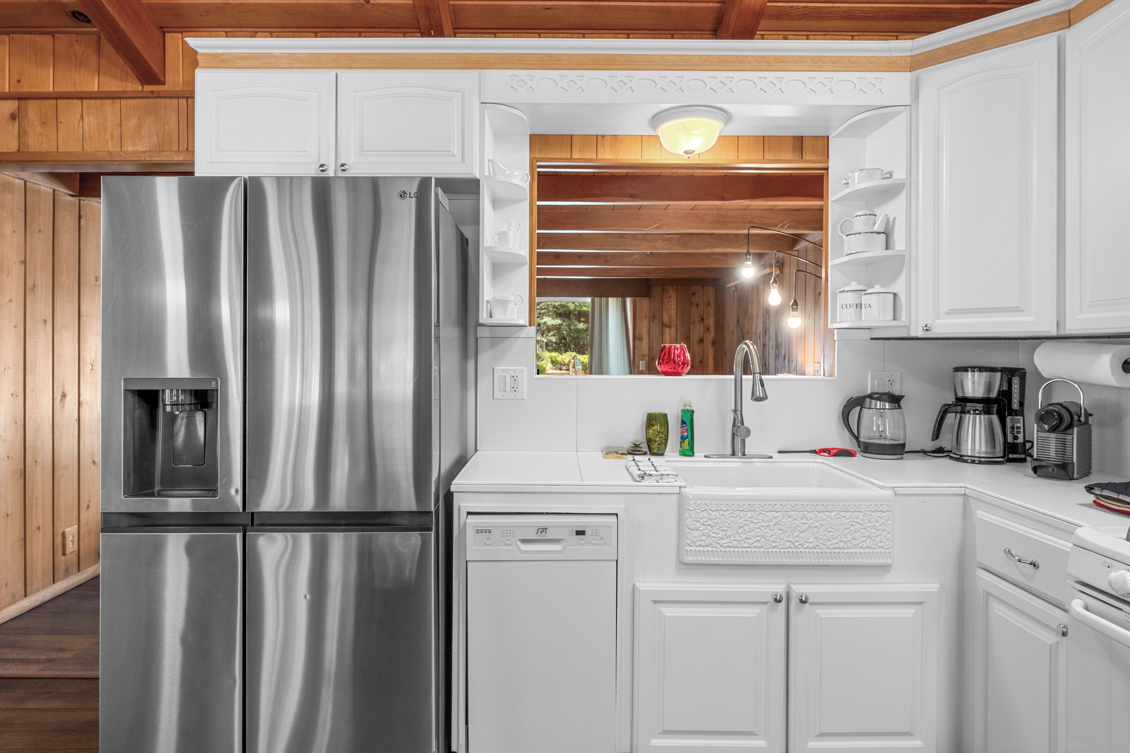 A modern kitchen with stainless steel appliances, white cabinetry, and a wooden ceiling.