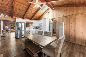 A wooden interior with a dining table, chairs, a kitchen area, and a ceiling fan. - Hot Tub! Walk to Village, & Trolley | Fenced Yard + Pet Friendly (Big Bear Lake)