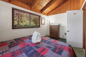 A bedroom with a wooden ceiling, a bed with a quilt, a dresser, a window with blinds, and a door. - Hot Tub! Walk to Village, & Trolley | Fenced Yard + Pet Friendly (Big Bear Lake)