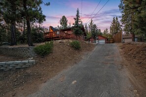 A paved driveway leading to a wooden cabin with a covered porch and a fenced yard. - Hot Tub! Walk to Village, & Trolley | Fenced Yard + Pet Friendly (Big Bear Lake)