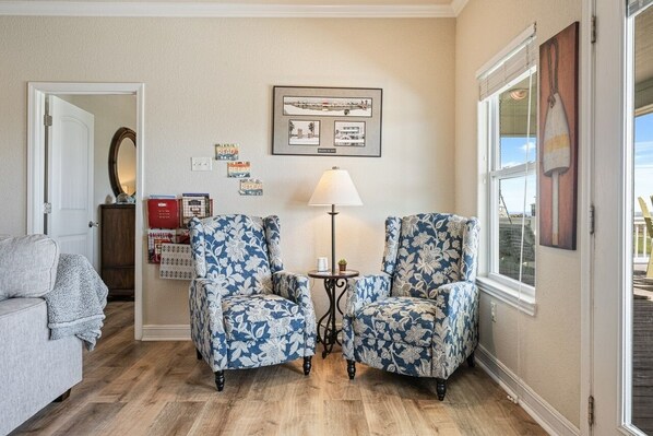 Une pièce comprenant deux fauteuils à motifs, une petite table avec une lampe, une carte encadrée accrochée au mur et une fenêtre donnant sur un paysage.