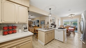A kitchen with a central island, wooden cabinets, and a dining area with a red tablecloth. - The Peacock Villa 5 Bedroom Home (Las Vegas)