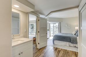A bedroom with a bed, a bathroom with a sink, and a door leading to a balcony. - Sunset Rentals | Barrington Arms 102 (Hilton Head Island)