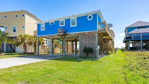 A two-story building with a blue exterior, a covered patio area, and a grassy lawn. - Crystal Blue 3 Bedroom Home (Port Bolivar)