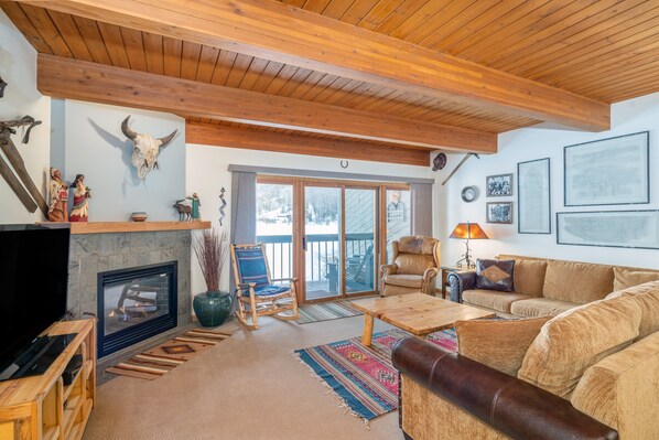 A cozy living room with a fireplace, wooden ceiling, and a large couch. - Ajax Vista at Riverside 2 Bedroom Condo (Telluride)