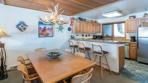 Una cocina con armarios de madera, una zona de comedor con mesa y sillas de madera, una araña y una isla de cocina.