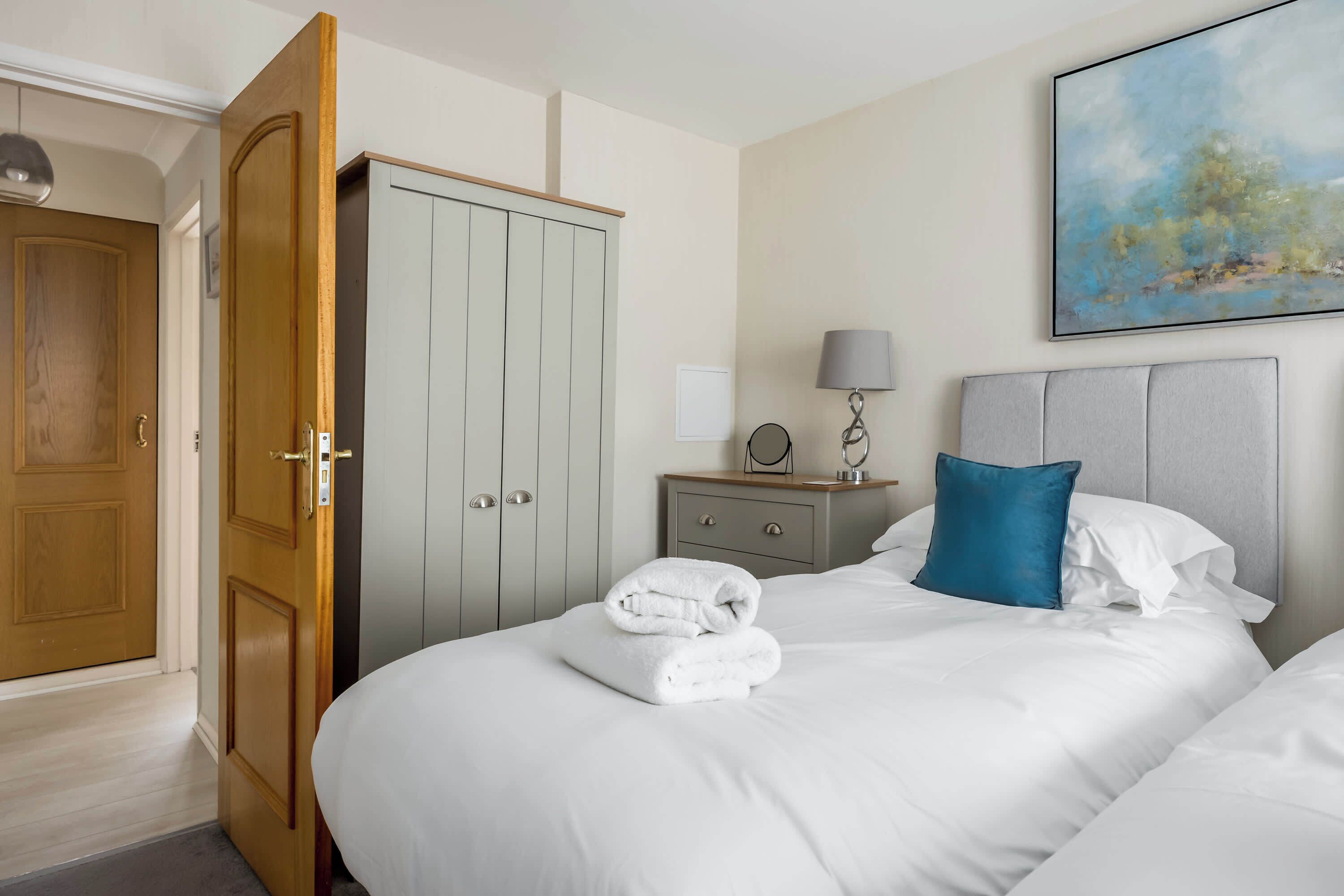 A hotel room with a bed, a wardrobe, a bedside table with a lamp, and a painting on the wall.