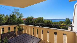 Ein Balkon mit Tisch, Stühlen, einer Topfpflanze und Blick auf das Meer und Bäume.