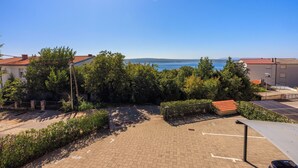 Ein gepflasterter Innenhof mit Blick auf das Meer, umgeben von Grünflächen und Gebäuden mit roten Dächern.