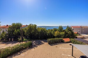 A paved courtyard with a view of the sea, surrounded by greenery and buildings with red roofs. - Vacation apartment for 2-5 people with sea view (Dramalj)