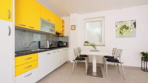 Eine moderne Küche mit gelben und weißen Schränken, einem Esstisch mit Stühlen, einer Uhr und einem Fenster mit Jalousien.