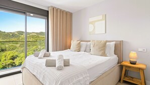 Un letto grande con vista sul verde esterno, un comodino in legno con una lampada e un moderno quadro a parete.