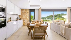 Una cucina moderna con mobili bianchi, una parete d'accento in pietra e un'area pranzo con un tavolo in legno apparecchiato per quattro persone.