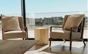 Two armchairs with woven cushions, a wooden side table, and a view of a hillside through large windows. - Luxury penthouse with sea views and pool near Marbella (Estepona)