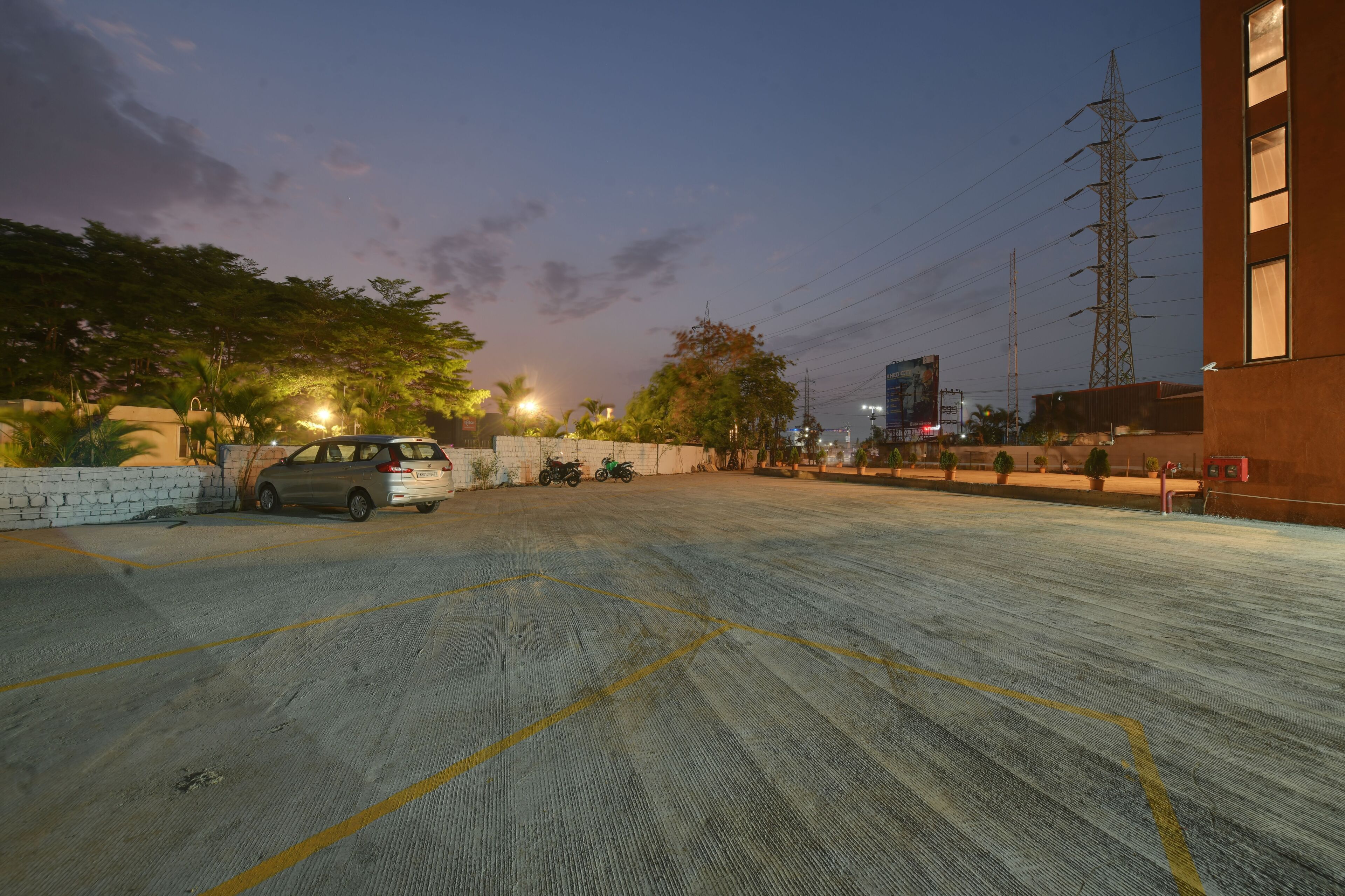 A parking lot with a car and motorcycles, surrounded by trees and buildings.