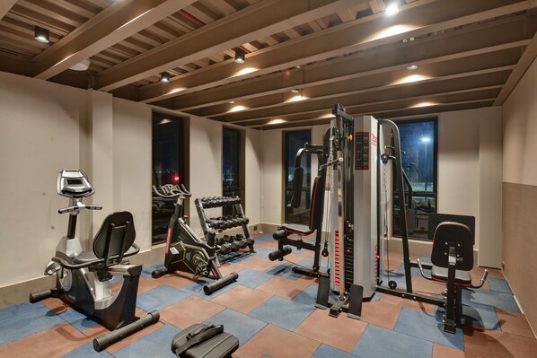 A gym with exercise equipment, a mirror, and a window with a view. - Click Hotels Lite Chakan (Rajgurunagar)