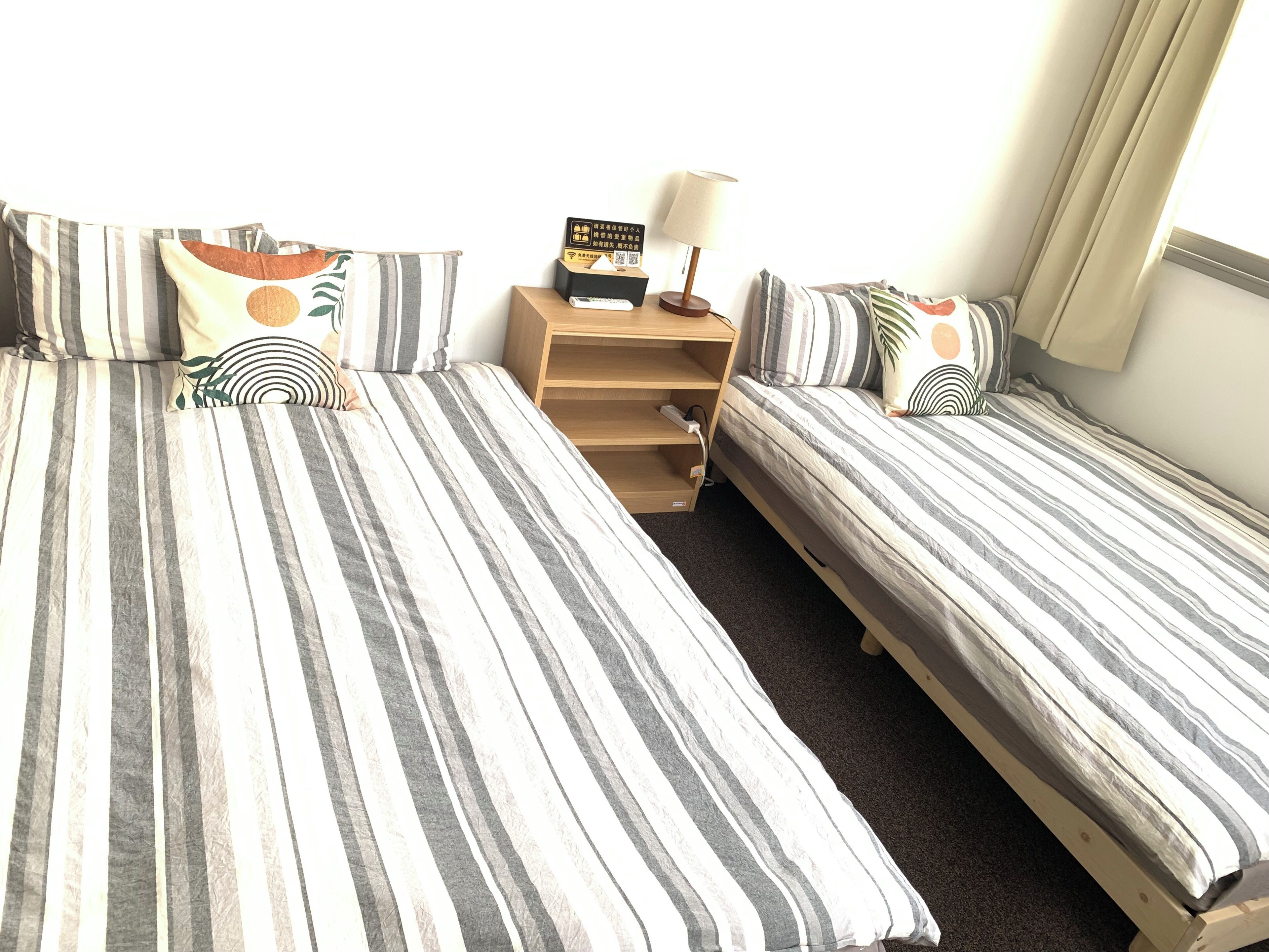 A room with two beds, a nightstand, a lamp, and a small table with a book and remote control.