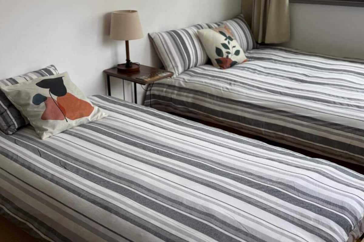 Two beds with striped bedding, a bedside lamp, and a window with curtains.